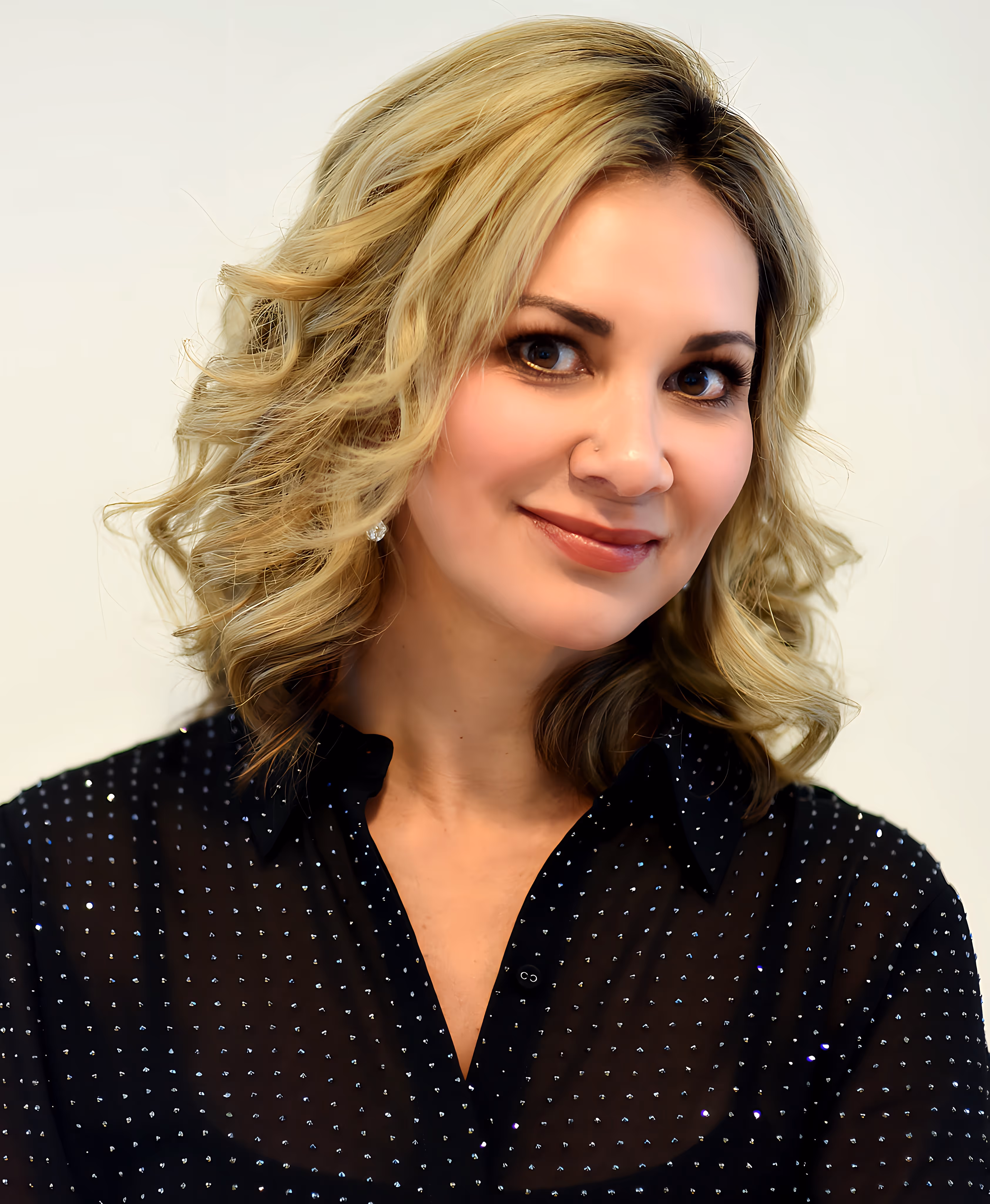 Smiling woman with blonde wavy hair wearing a black blouse with small white dots.