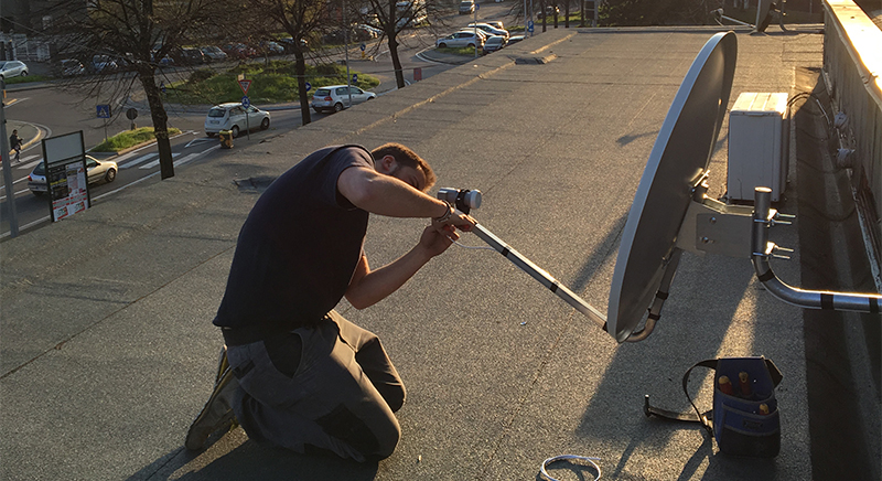 Man kneeling on a rooftop installing a satellite dish during sunset.