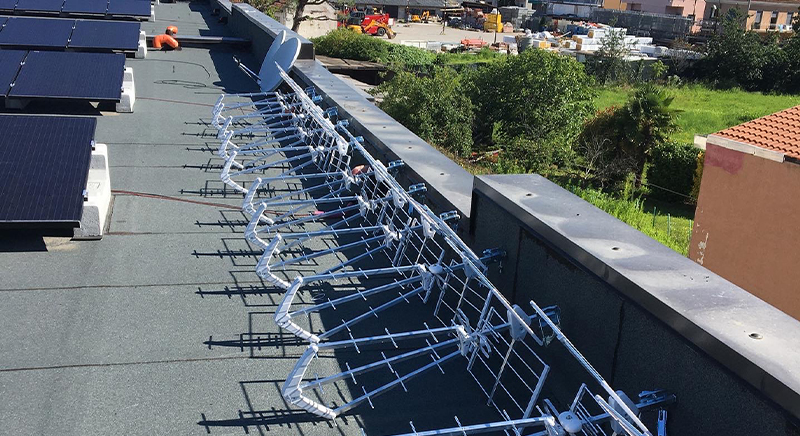 Rooftop with solar panels on the left and a row of large, metallic antenna structures mounted along the edge.