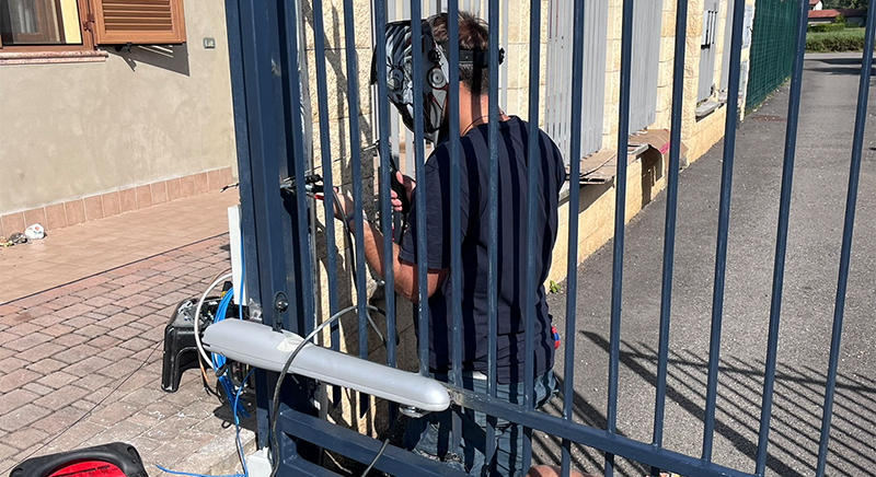 Man wearing a virtual reality headset standing behind a metal fence on a paved sidewalk next to a building.