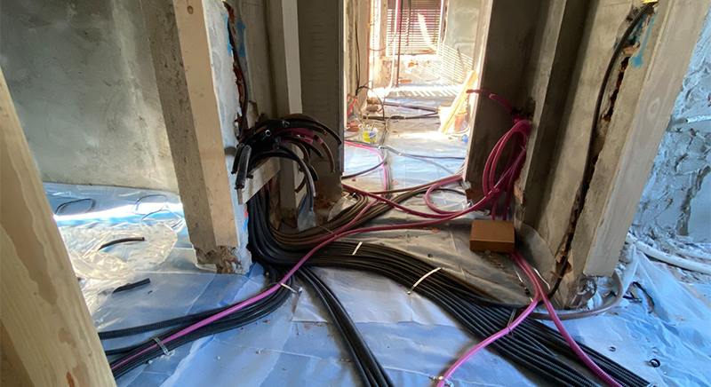 Electrical conduit pipes and cables laid out on a plastic-covered floor in a building under construction.