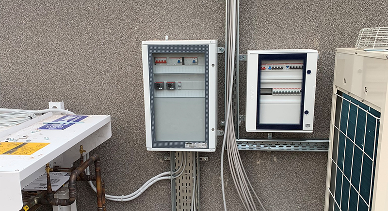 Two views of a utility room with red expansion tanks, pipes, electrical control boxes, and a white boiler mounted on the wall.
