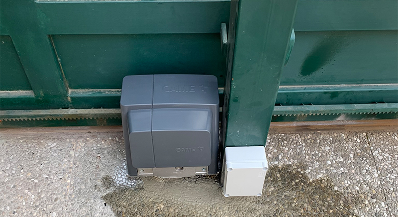 Close-up of an automatic sliding gate motor system installed on a concrete base between two concrete fences.