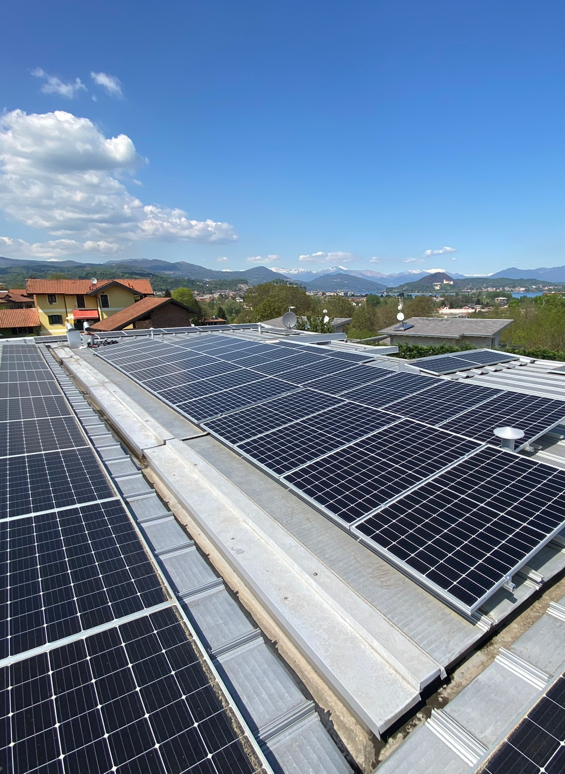 Solar panels installed on a rooftop with a scenic background of houses, trees, and mountains under a blue sky.