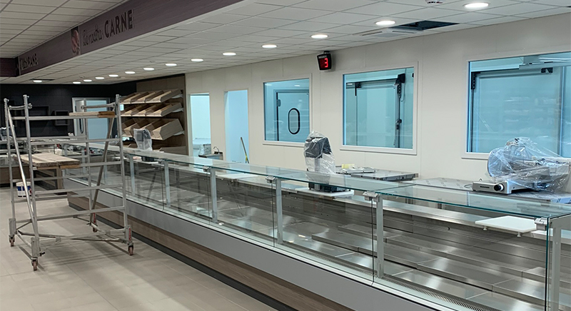 Empty refrigerated display cases and metal shelving inside a modern grocery store or deli under construction.