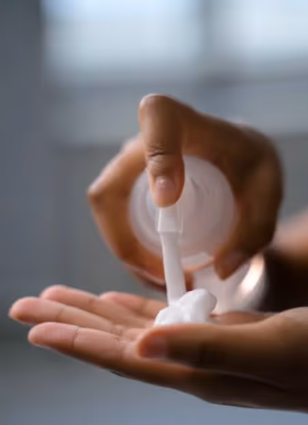 Person's hands pumping a mouse cosmetic product in their hand.
