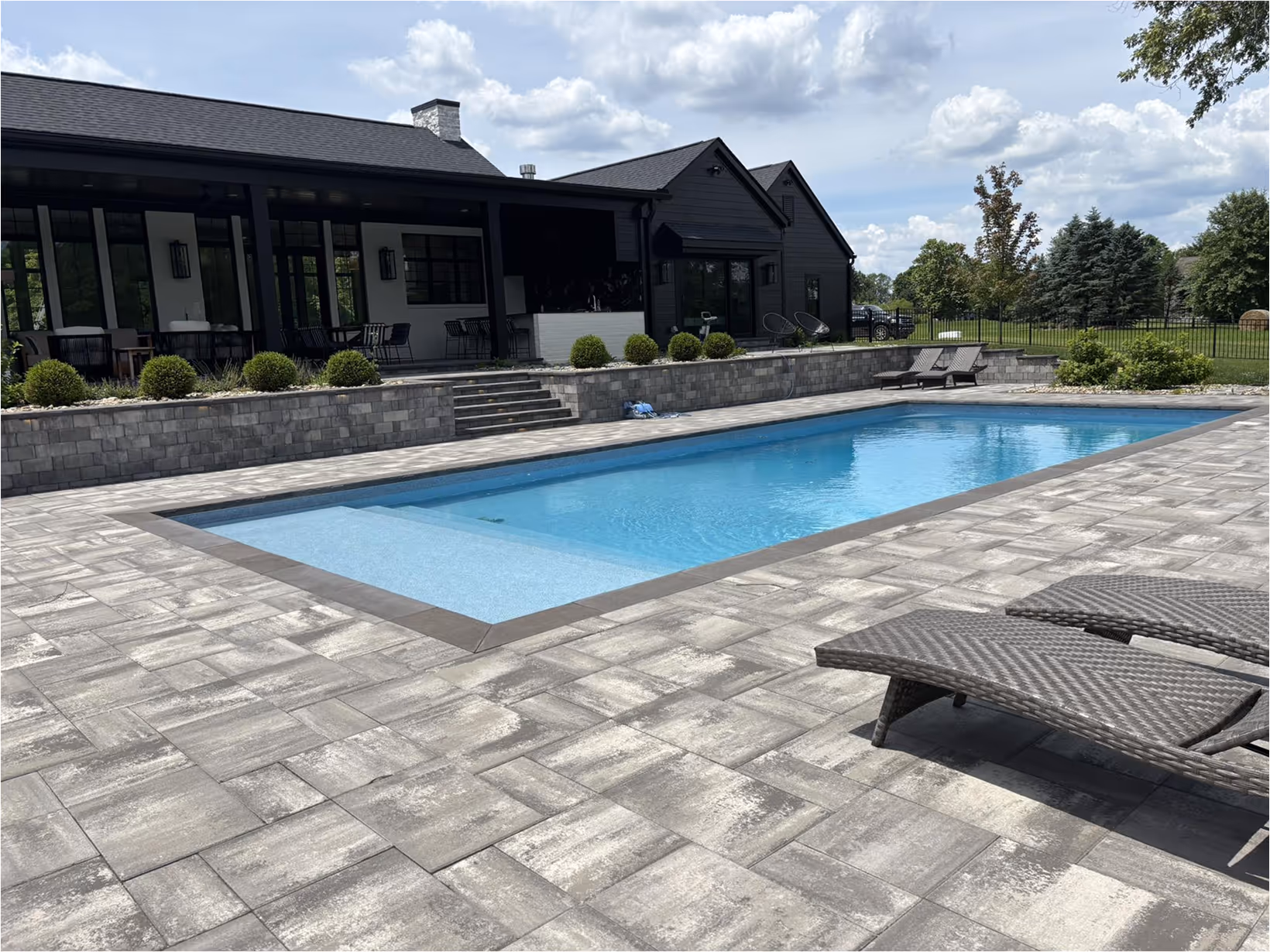 Pool in back yard with grey tile on ground behind house