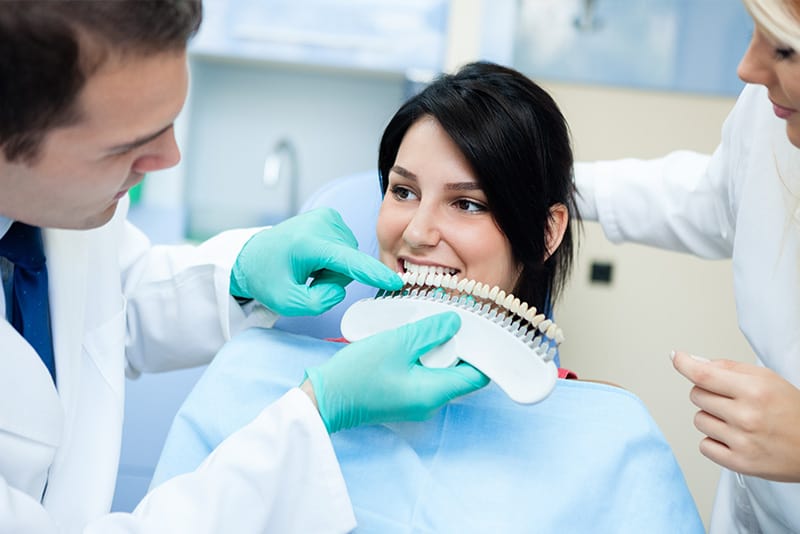 Dentist holding a shade guide near patient's teeth prior to teeth whitening session.
