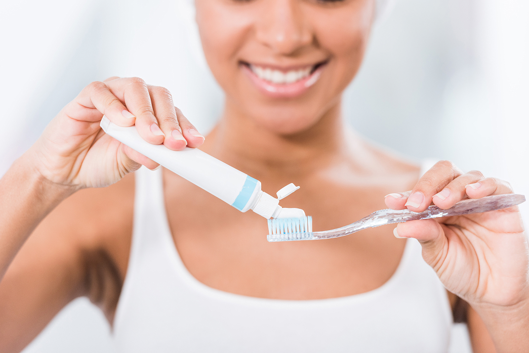 Woman applies toothpaste to a toothbrush as part of her daily preventive dental care routine.