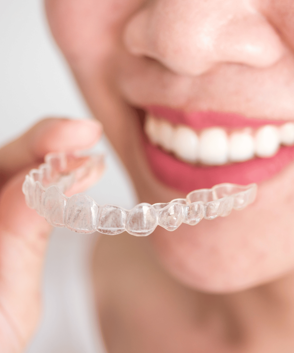Patient holds a clear dental aligner in front of her smile.