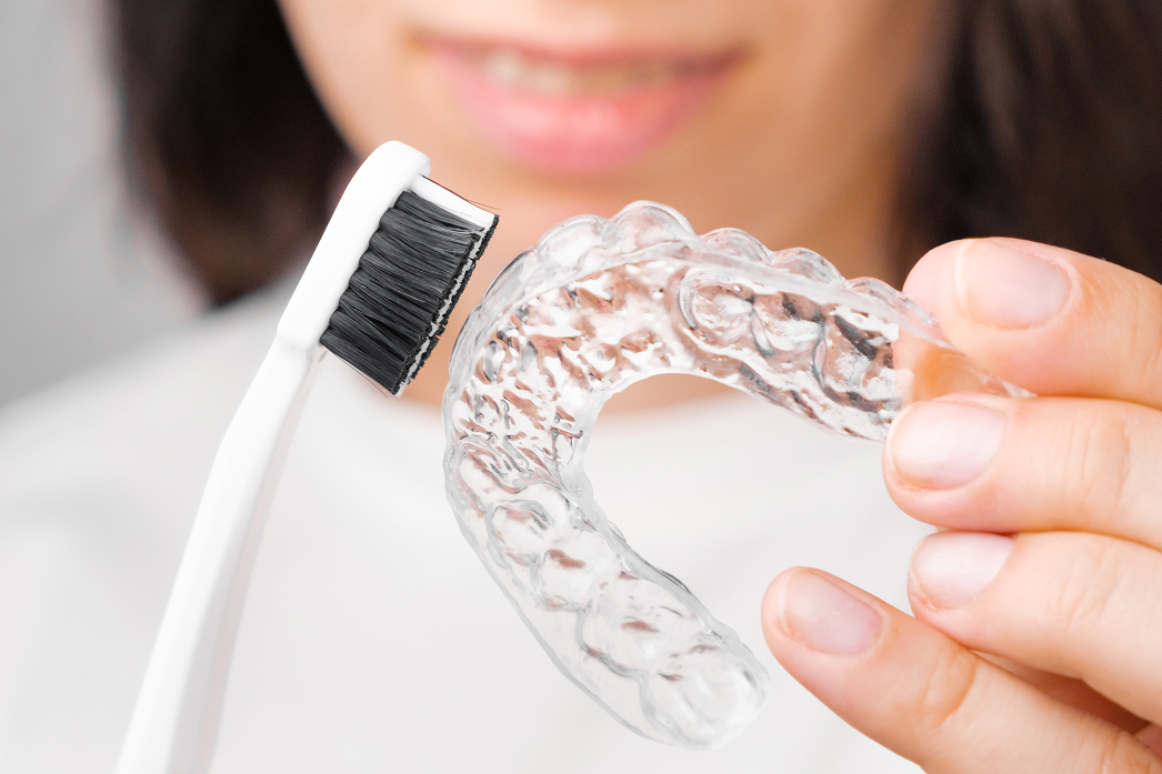 Patient cleans a clear dental aligner with a toothbrush.