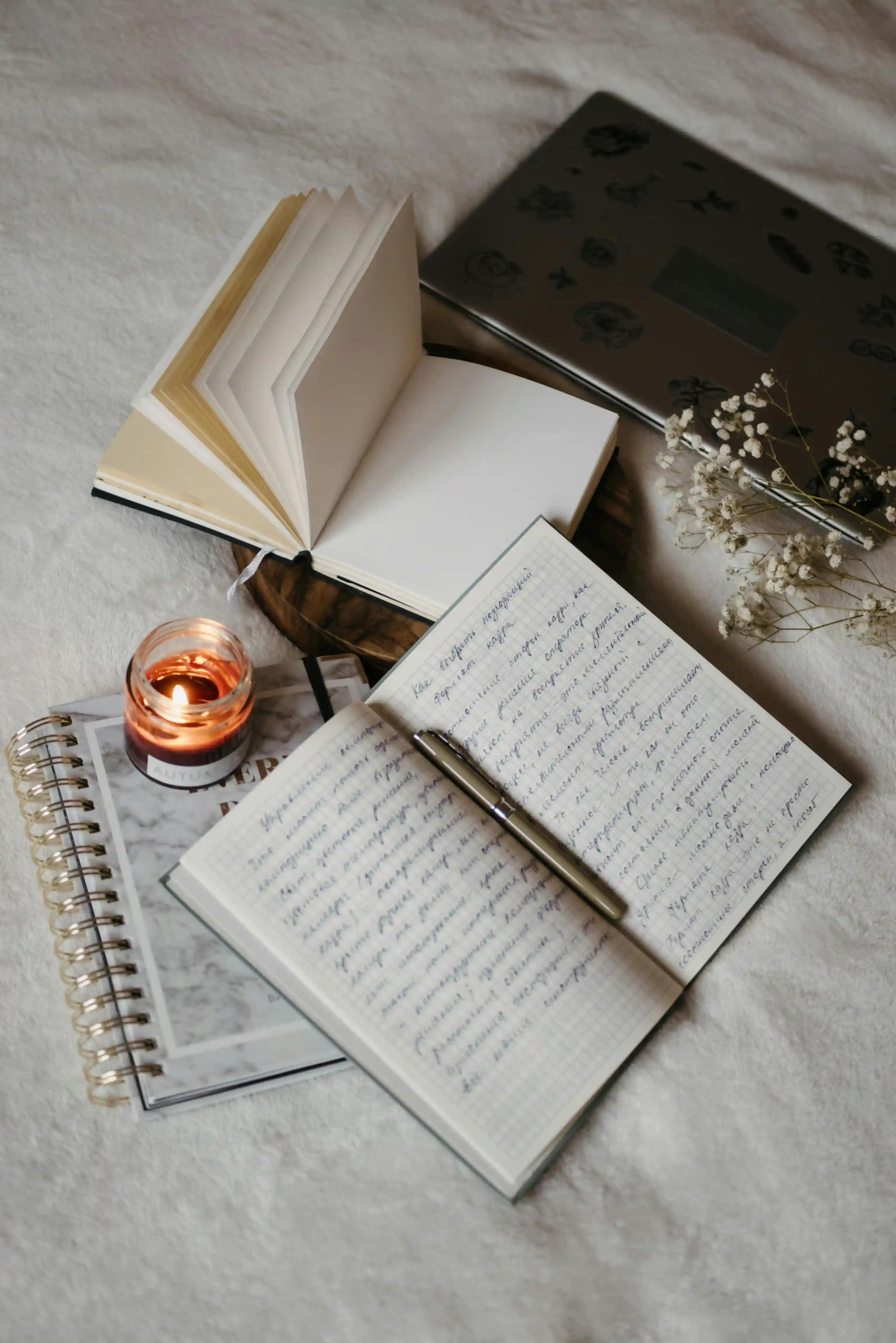 Open journal on bed with lit candle by its side.