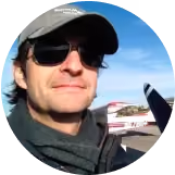 A man wearing sunglasses and a hat is standing in front of a plane. - Forme Images