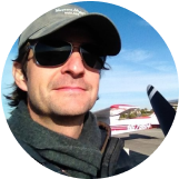 A man wearing sunglasses and a hat is standing in front of a plane. - Forme Images