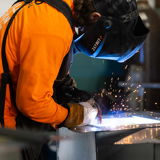 Worker welding metal with protective gear and sparks flying