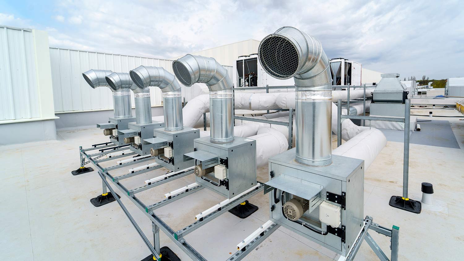 Commercial rooftop ventilation system with multiple metal exhaust ducts and fans