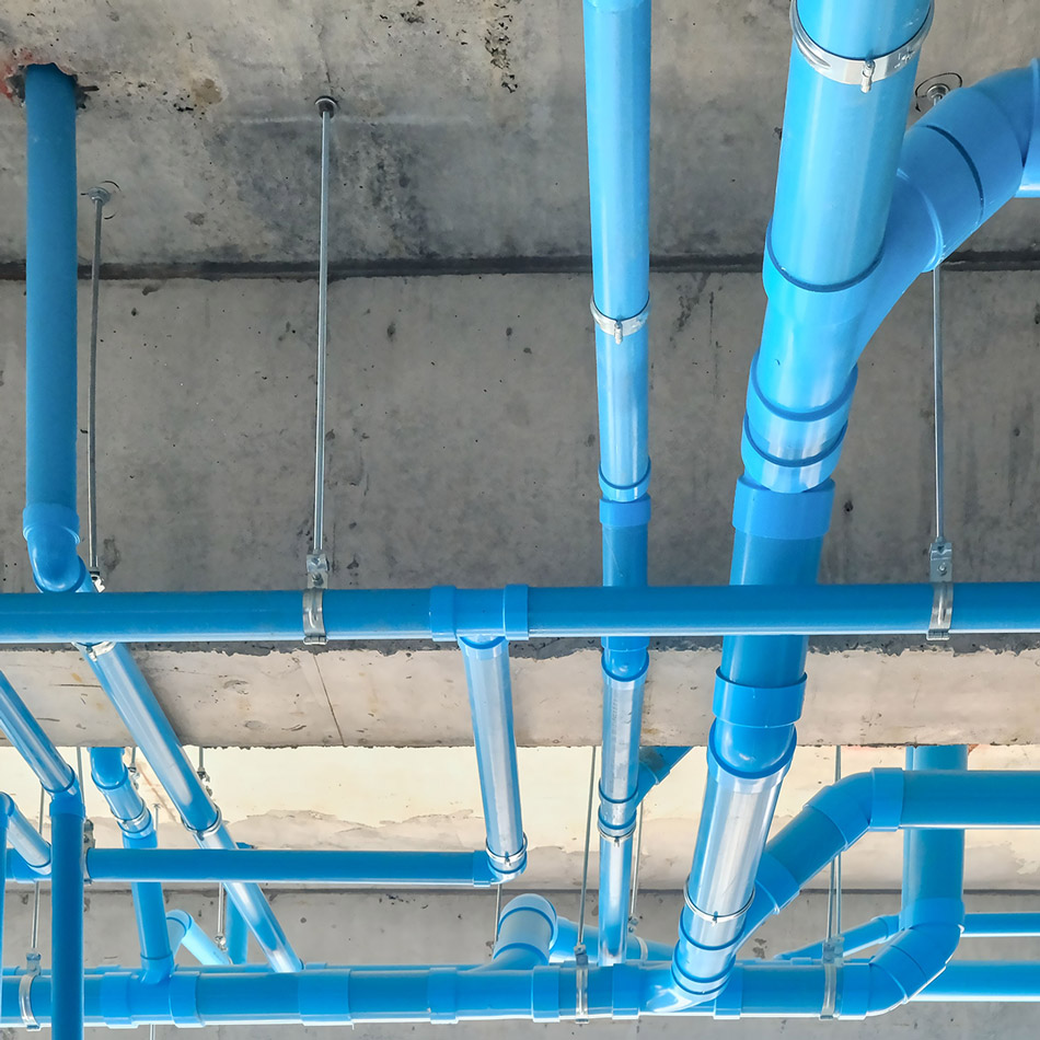 Blue PVC plumbing pipes installed along a concrete ceiling in a commercial building