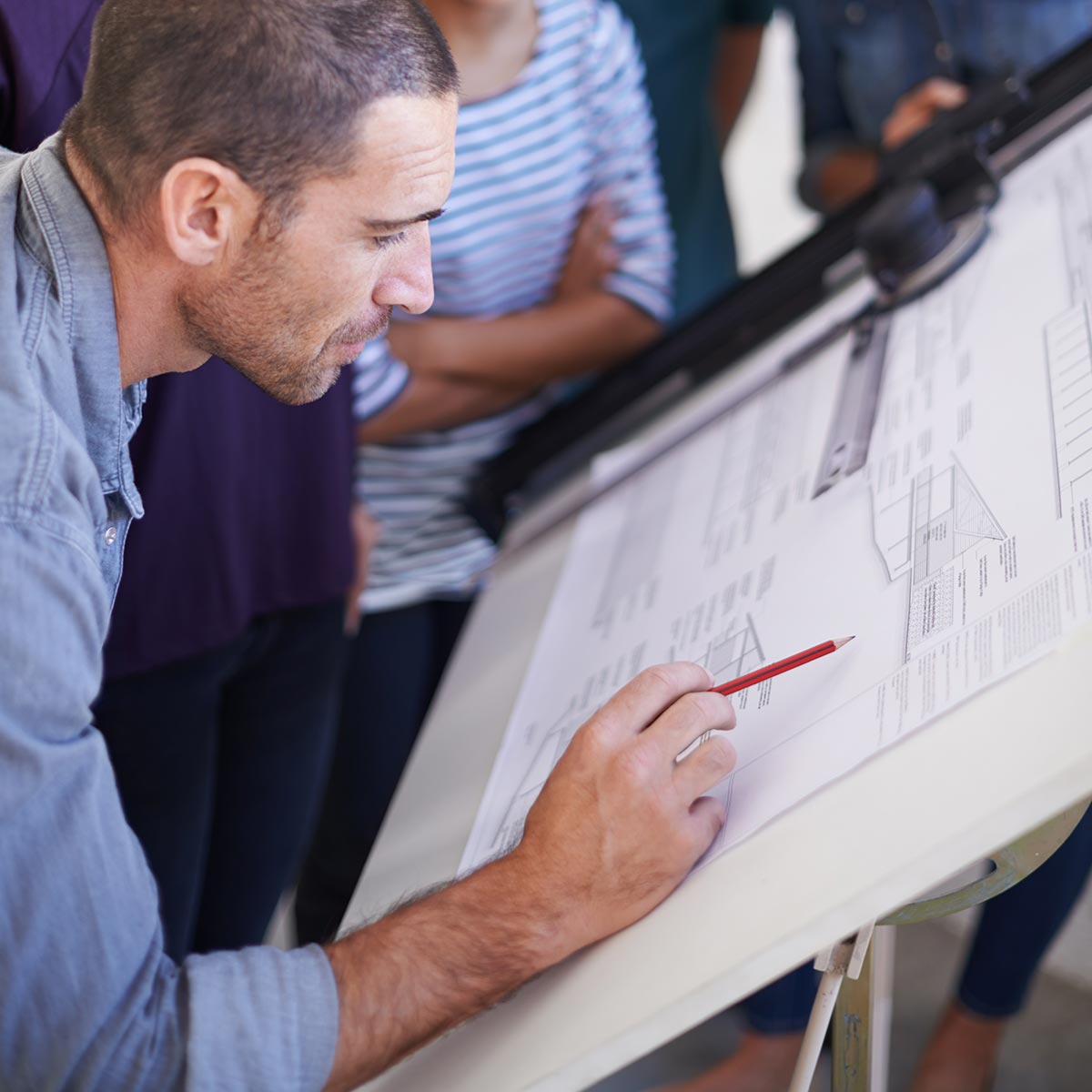 Workers reviewing detailed building plans with a team at a drafting table