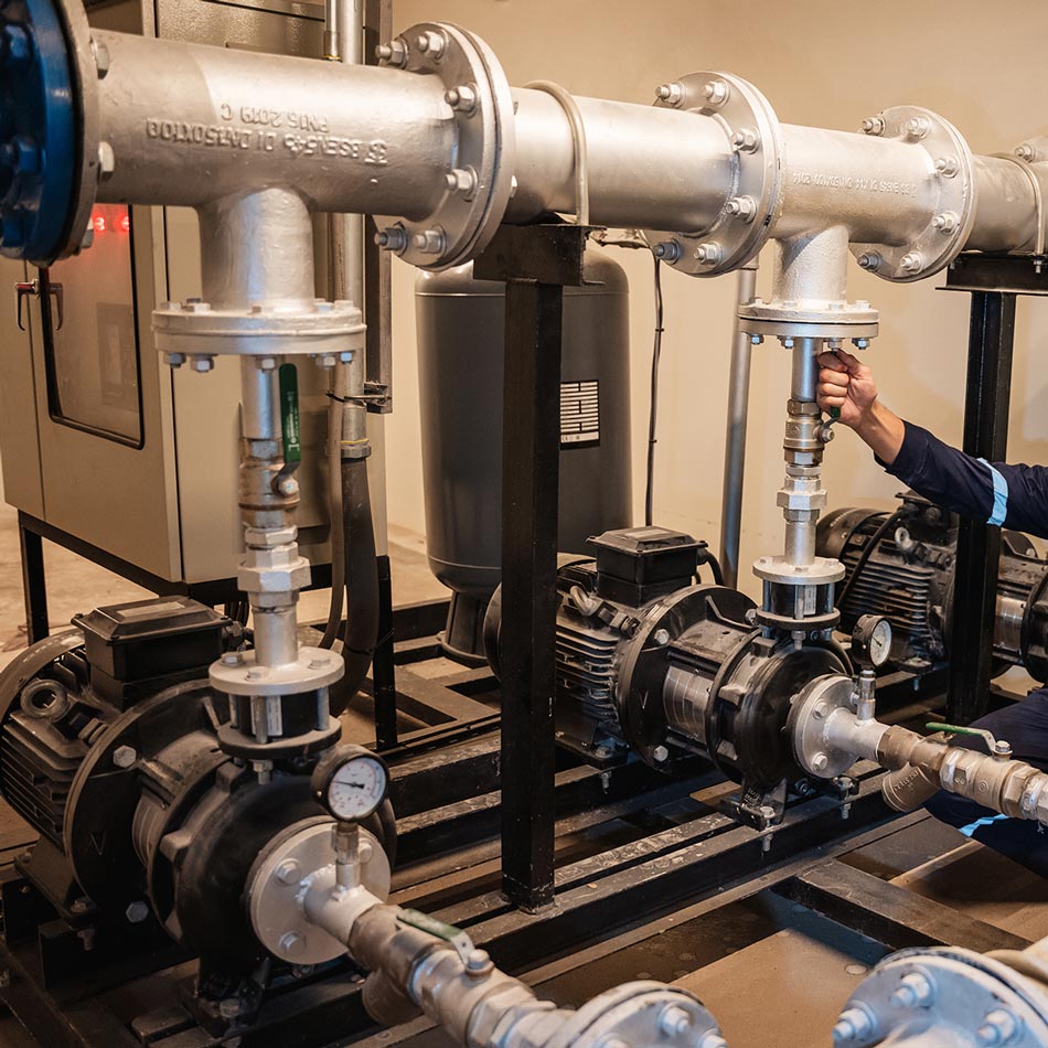 Commercial pump system maintenance with technician adjusting industrial piping
