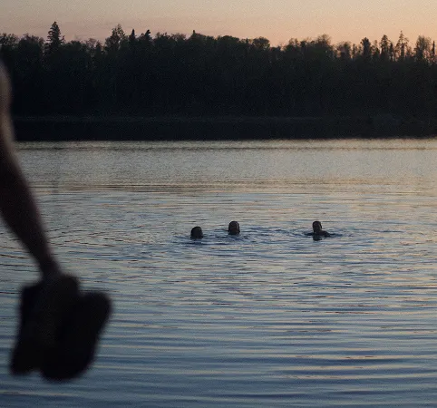 A group of people swimming in a lake at dusk.