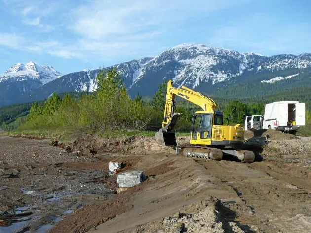 A larger digger working next to a creek in a mountain valley.
