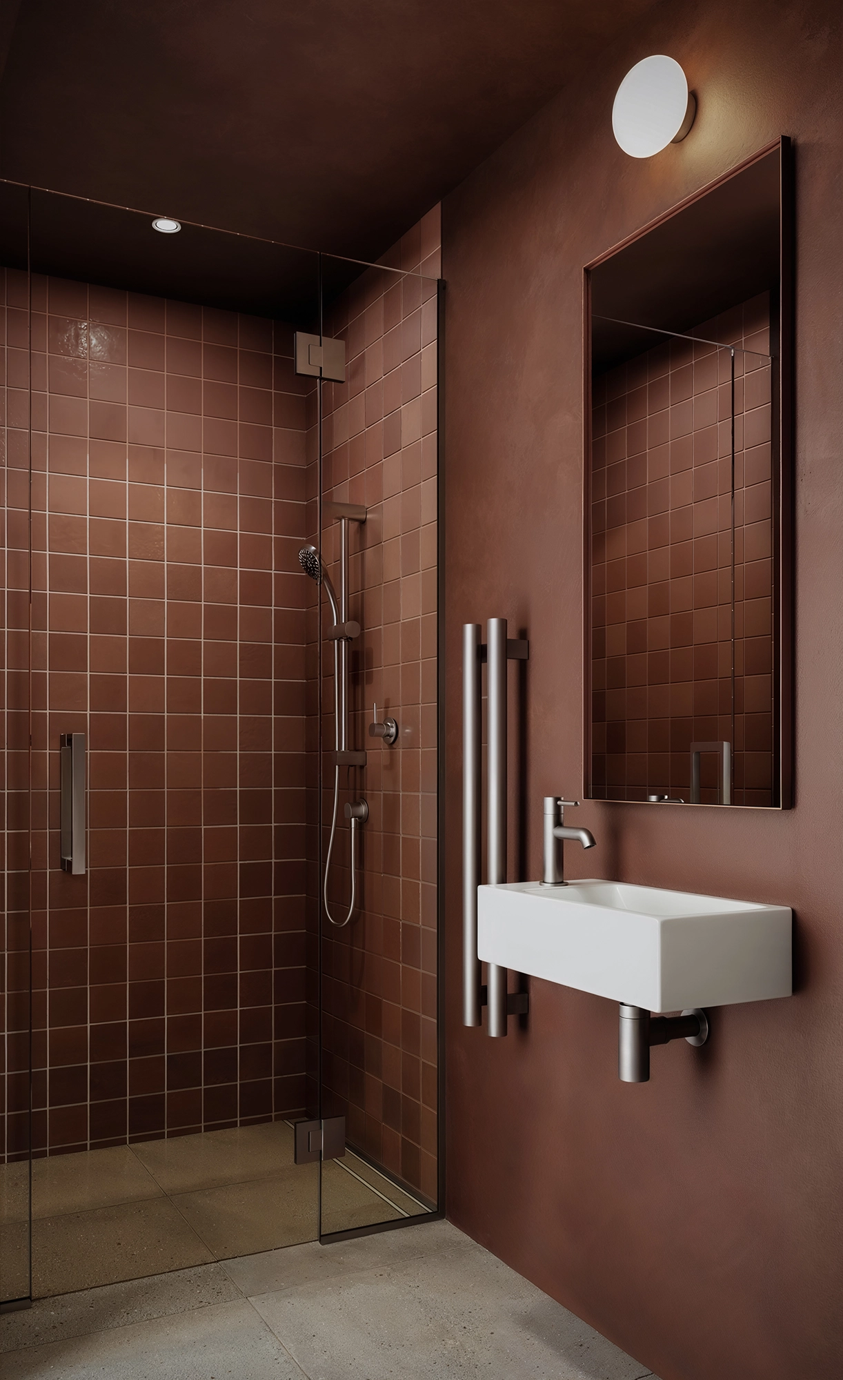 Modern bathroom with brown tiled shower, glass door, wall-mounted white sink, and rectangular mirror.