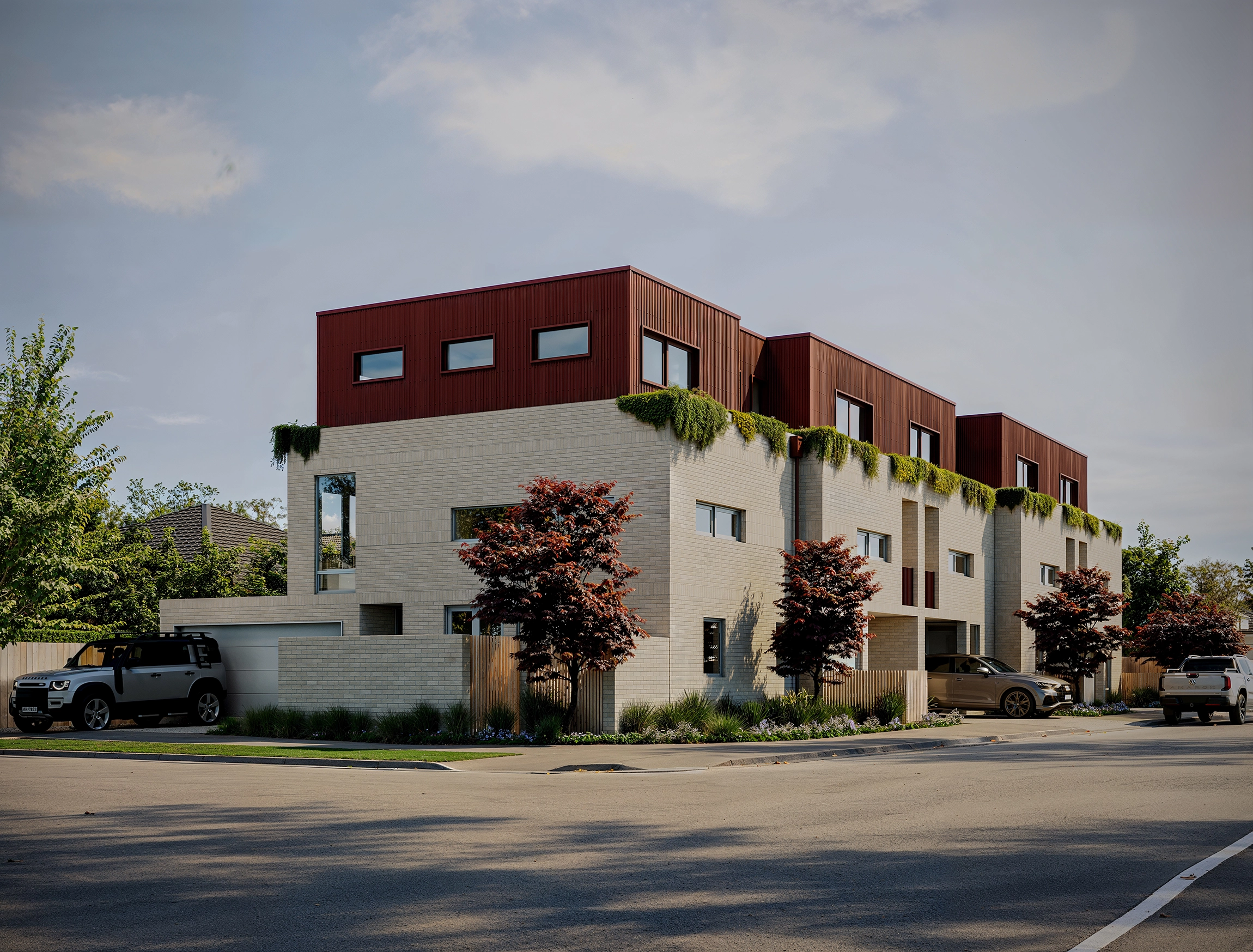 Modern residential corner building with beige bricks, red upper section, greenery, and parked cars.
