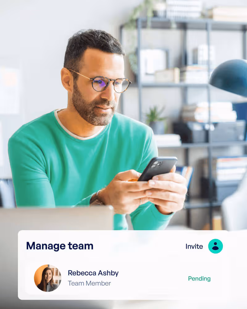 Man in glasses and green sweater managing a team on his smartphone with a pending invite for Rebecca Ashby displayed on screen.