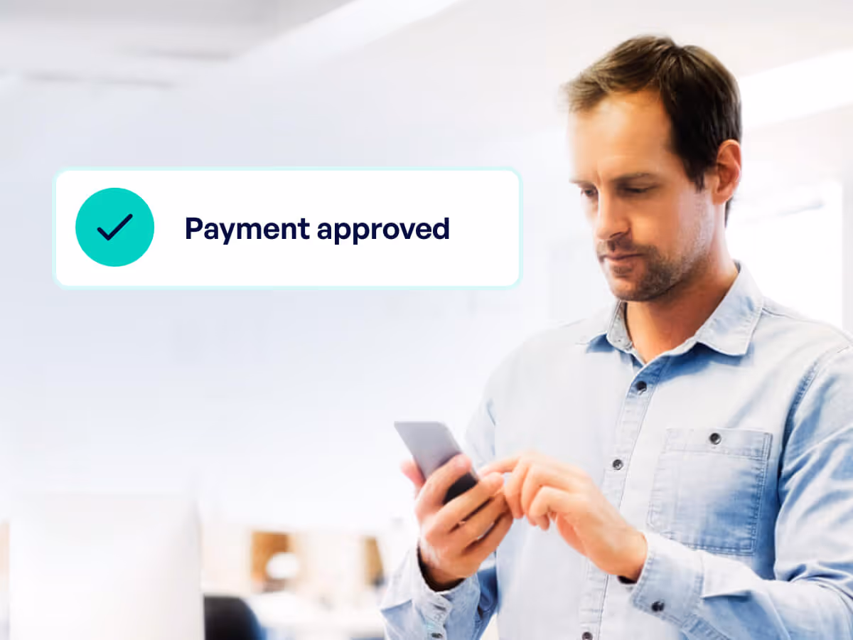 Man in a light blue shirt holding a smartphone with a screen message saying Payment approved and a checkmark icon.