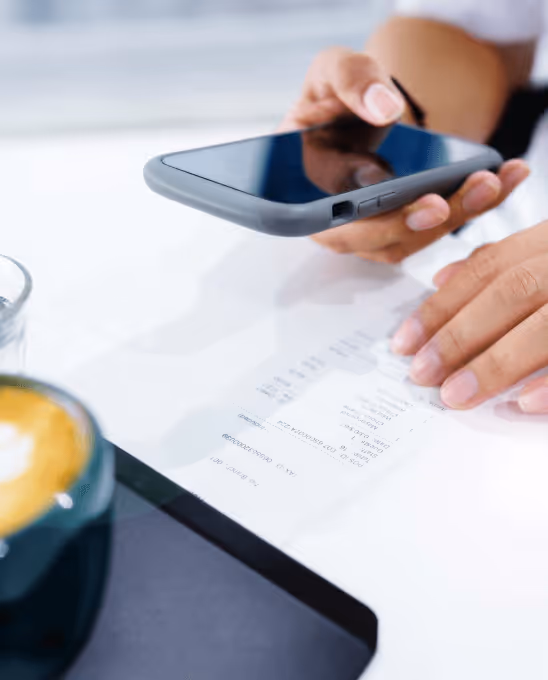 Person holding a smartphone over a white table with a receipt, near a cup of coffee.