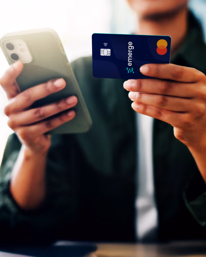 Person holding a smartphone in one hand and an Emerge Mastercard credit card in the other.