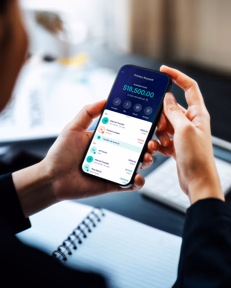 Person holding a smartphone displaying a banking app with a primary account balance of $18,500 and recent transactions.