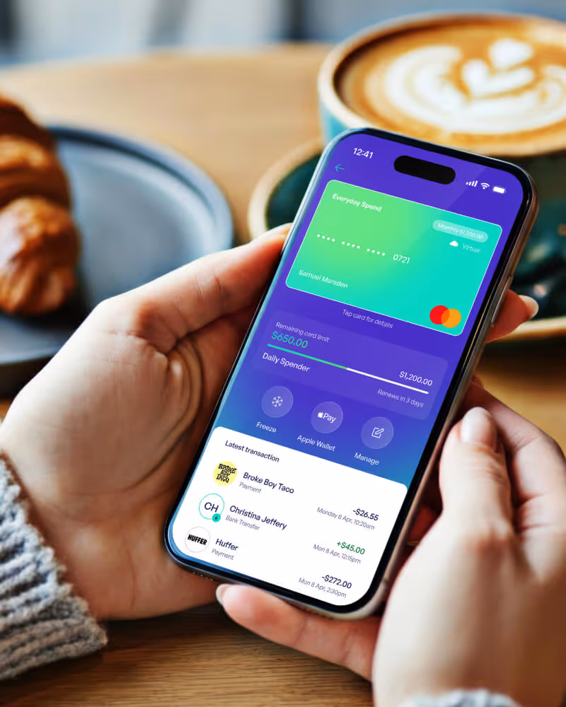 Person holding a smartphone displaying a personal finance app with card balance, spending limit, and recent transactions.