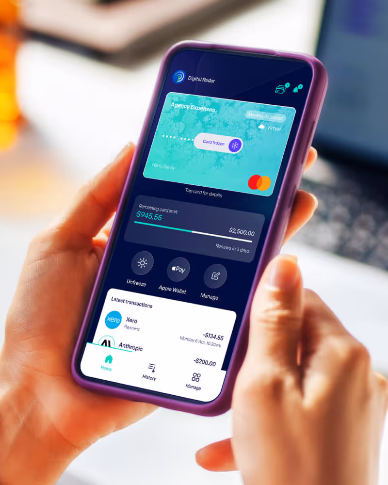 Hand holding a smartphone displaying a digital wallet app with a frozen virtual card named Agency Expenses and recent transactions.