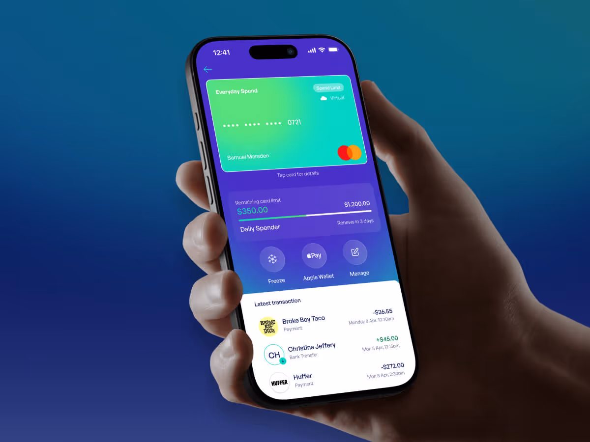 Hand holding a smartphone displaying a financial app with a digital Mastercard, remaining card limit, transaction history, and options to freeze card, use Apple Wallet, and manage account.