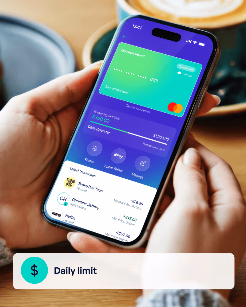 Person holding a smartphone displaying a financial app with a virtual card named Everyday Spend, showing a $350 remaining daily spend limit of $1,200 and recent transactions.