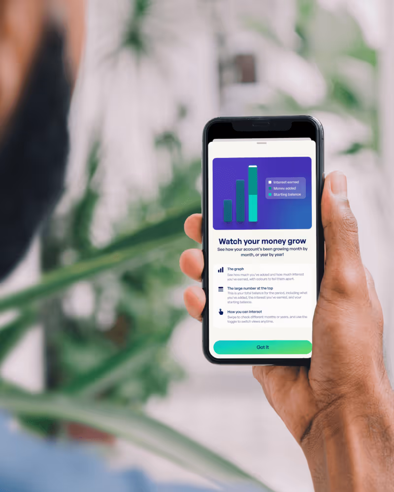 Hand holding a smartphone showing a financial app screen with a bar graph and instructions titled 'Watch your money grow'.