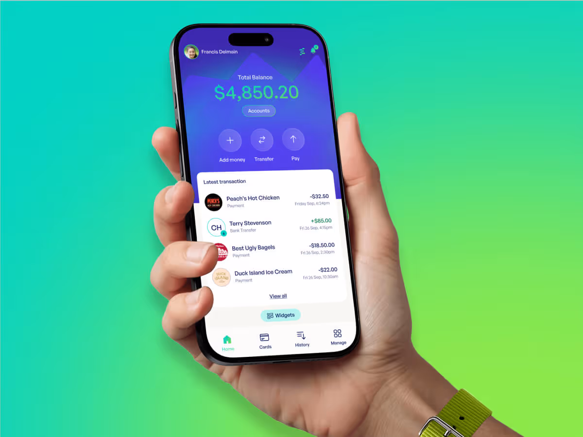 Hand holding a smartphone displaying a banking app with a total balance of $4,850.20 and a list of recent transactions.
