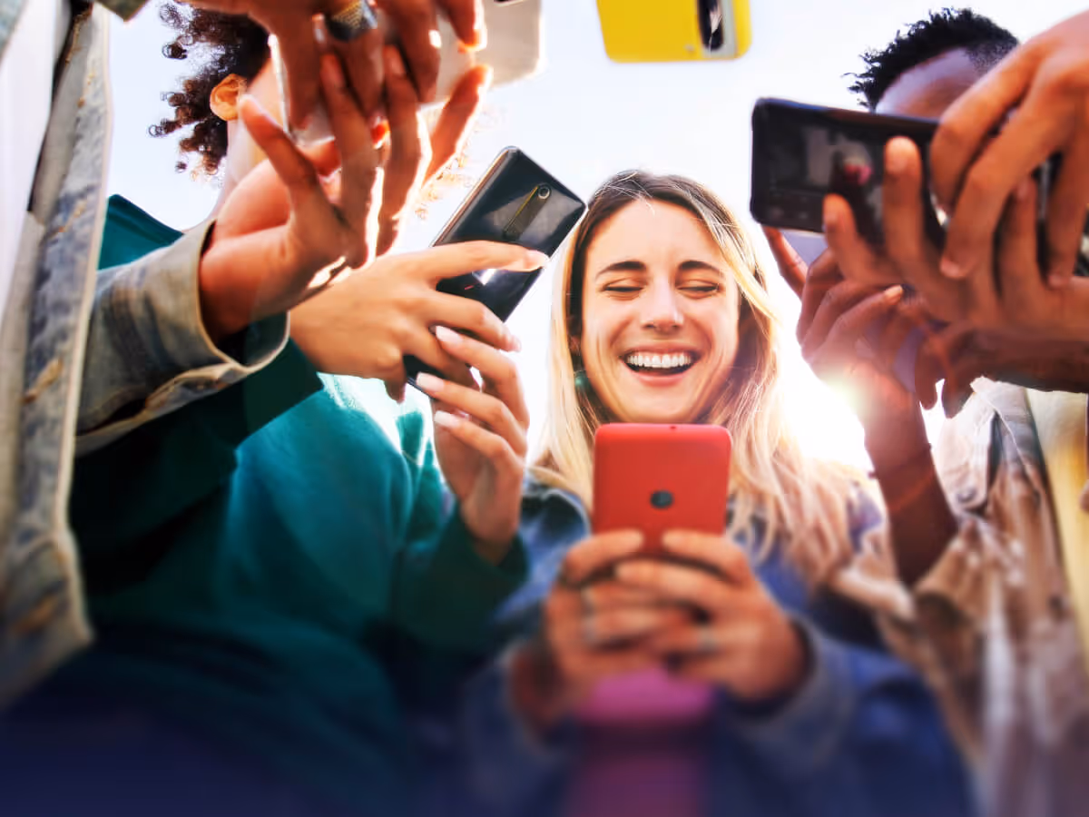 Group of diverse young people smiling and looking at their smartphones together.