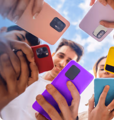 Group of diverse people holding colorful smartphones in a circle, viewed from below against a blue sky.