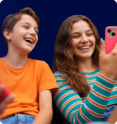 Two smiling teenagers, a boy in an orange shirt and a girl in a striped shirt, taking a selfie with a pink phone.