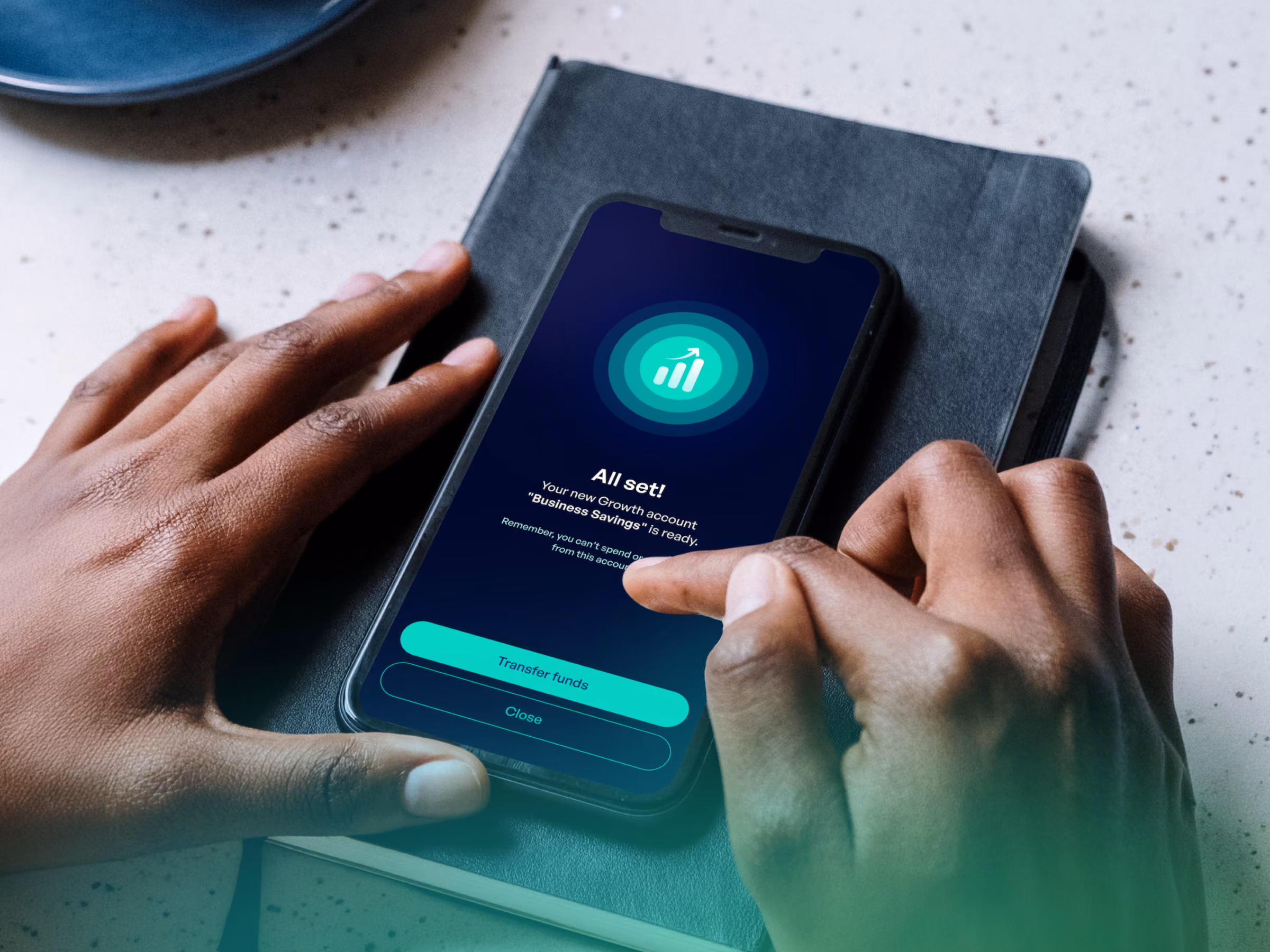 Hands holding a smartphone showing a business account setup confirmation with transfer funds and close buttons.