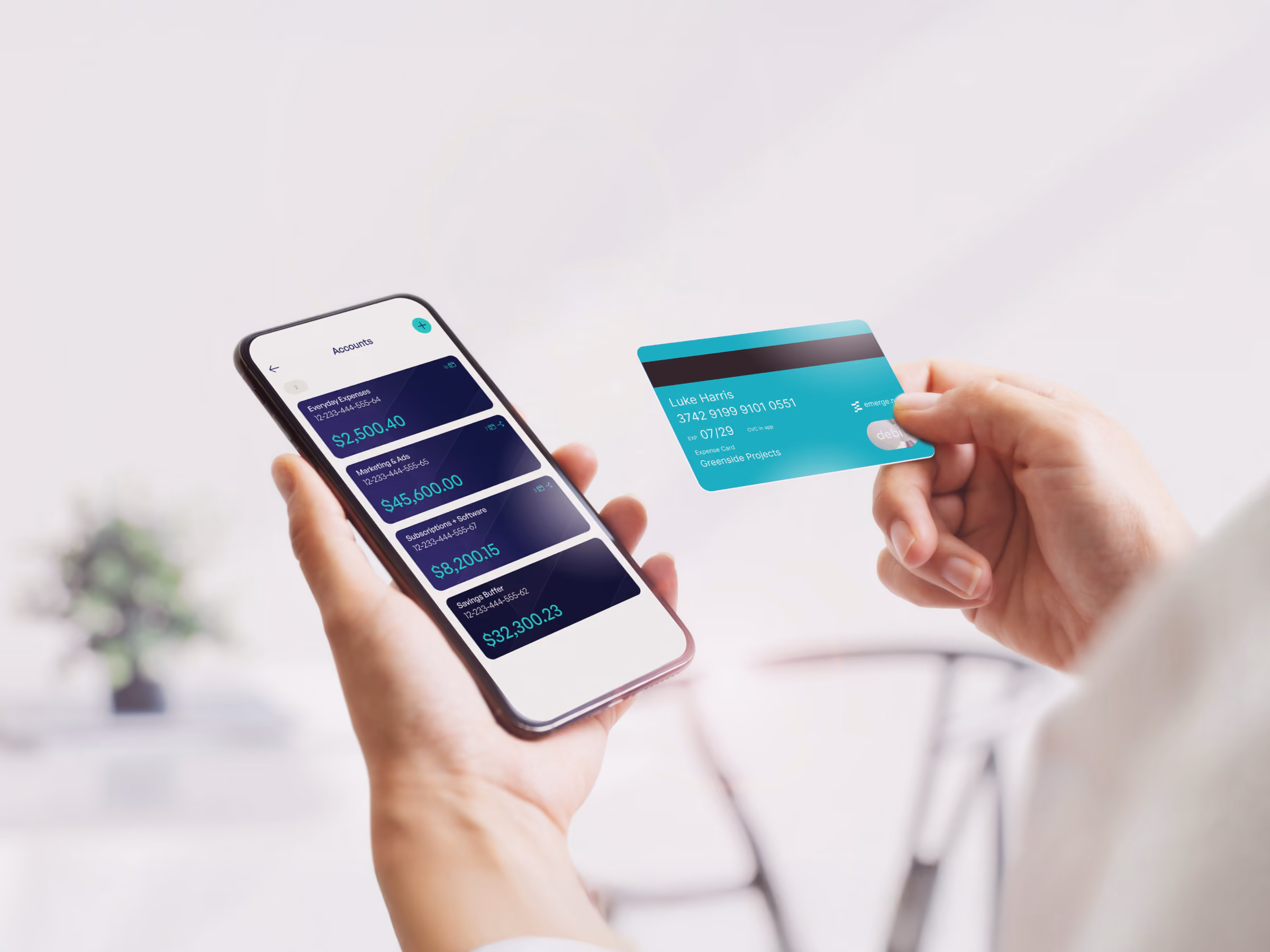 Person holding phone showing business account balances and a teal debit card with name and number.