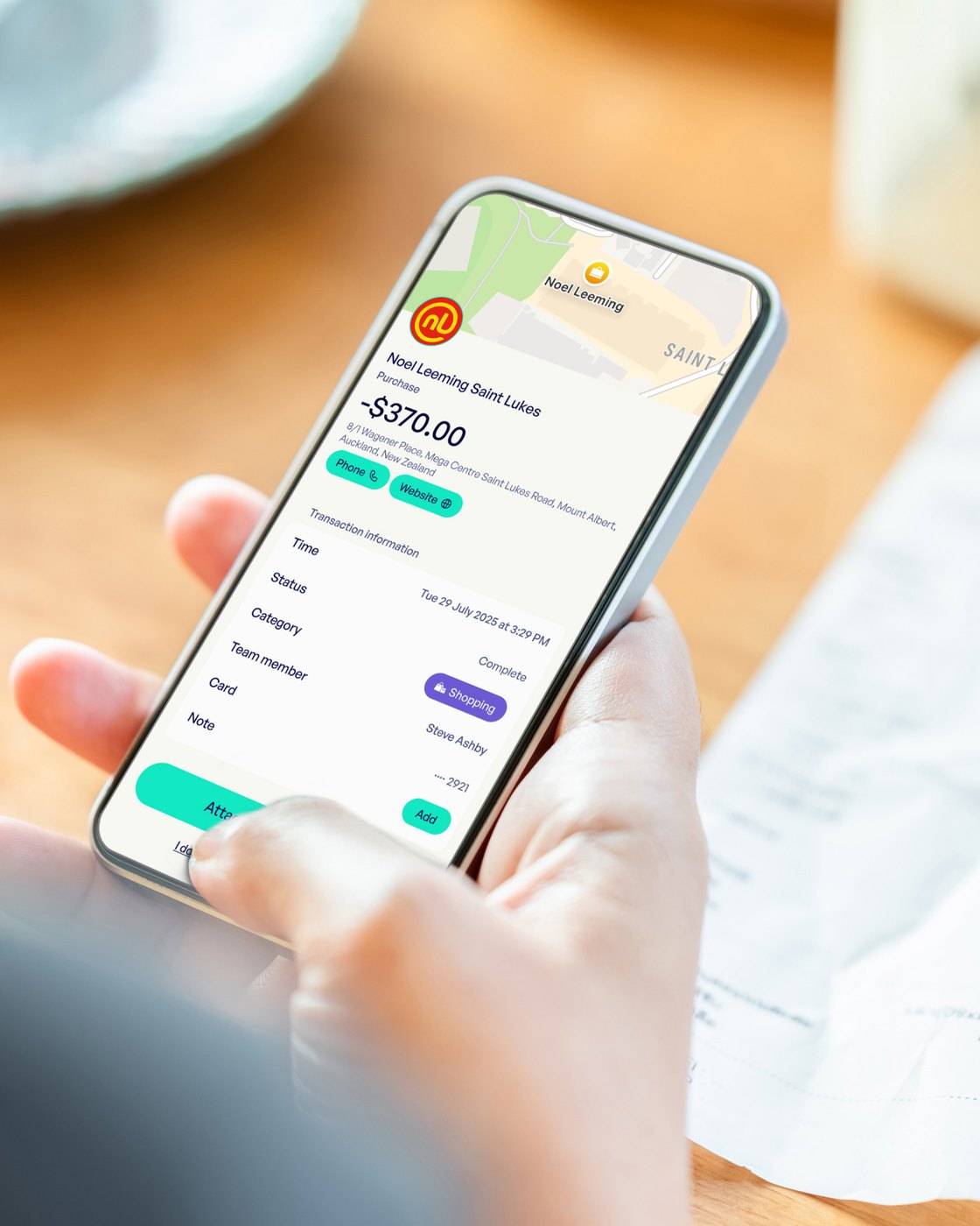 Hand holding a phone showing a transaction detail screen with a receipt attached.