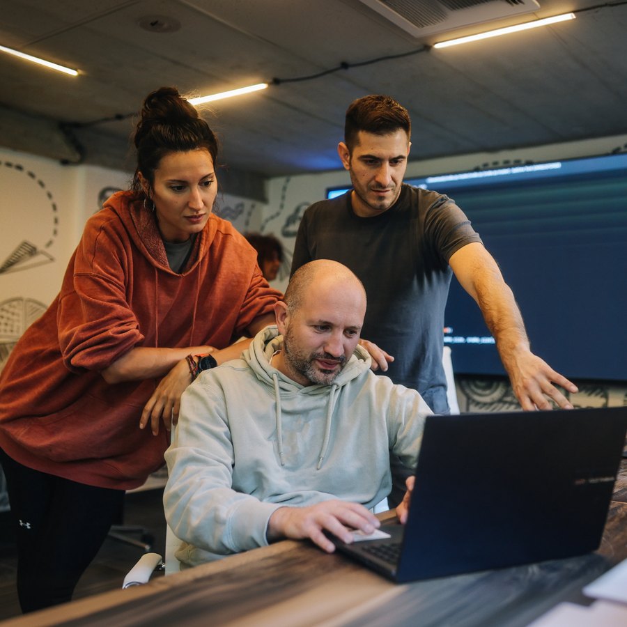 Three colleagues gathered around a laptop in a studio workspace.