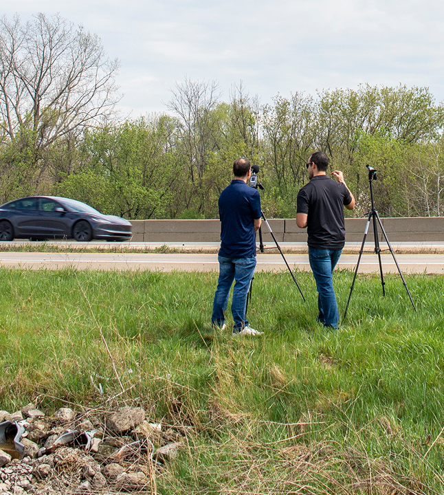 Two men testing noise outdoors with decibel meter microphones.