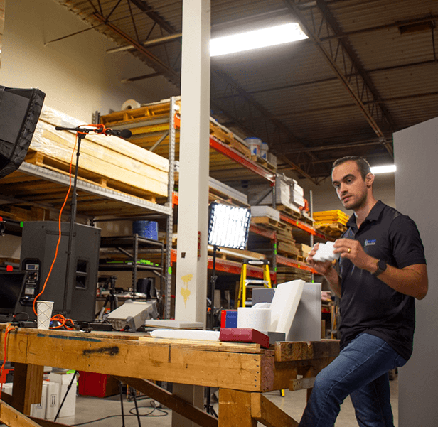 A Memtech Acoustical employee holds an acoustic pad inside a room filled with different equipment.