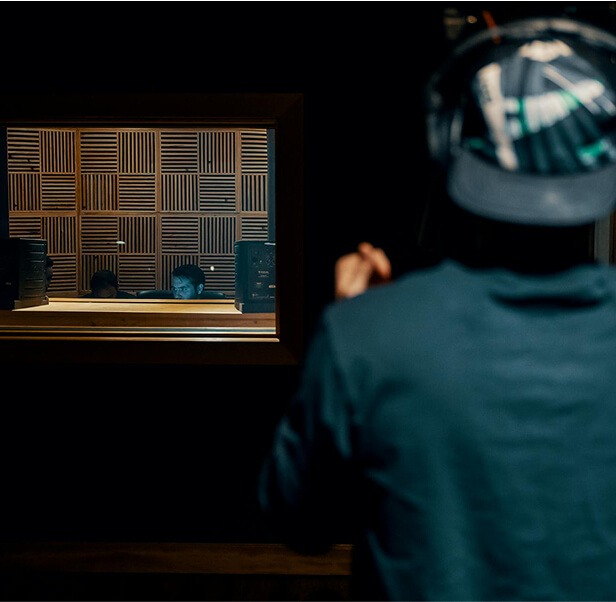 A man inside a studio room, while there are two men in the music room with acoustic pads.