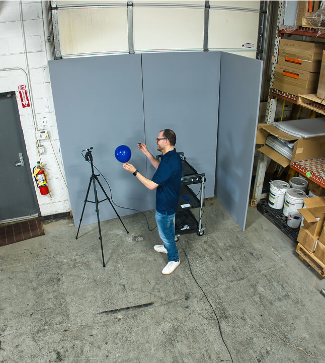 An employee of Memtech Acoustical testing popping a balloon in an area with acoustic pads towards a mic.