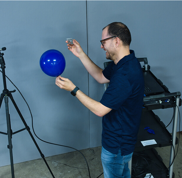 An employee of Memtech Acoustical testing popping a balloon in an area with acoustic pads towards a mic.